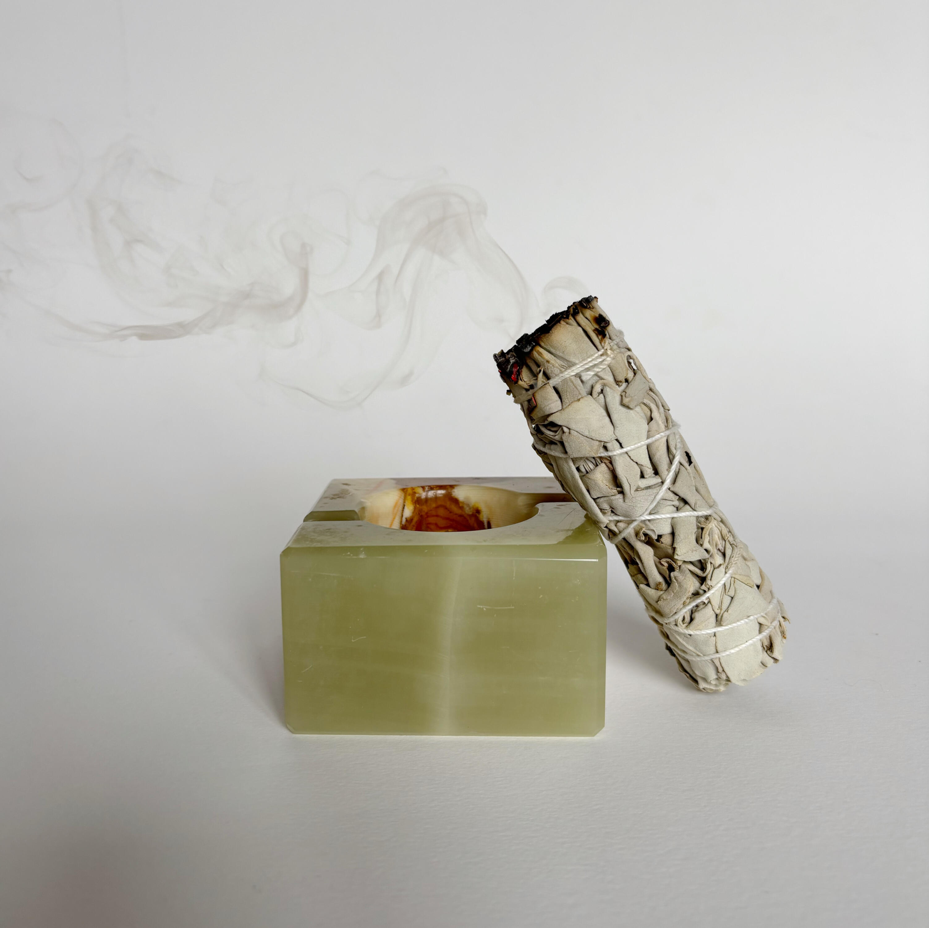 sage stick resting on a green stone holder with soft smoke